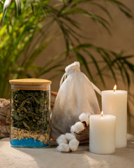 A table displays a jar of natural herbs and mine salts, a candle, and cotton bag full of herbal infusion, creating a tranquil setting ideal for relaxation and self-care rituals.