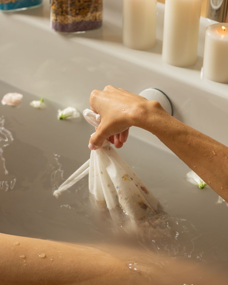 A serene bath scene featuring a person in a tub adorned with flowers, infusing the water with a calming bath tea blend.